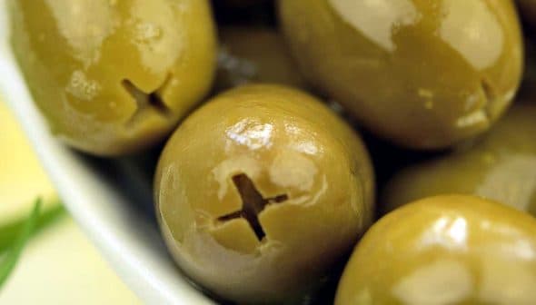 Close-up of green olives in a white bowl with a glossy surface. - Olive Oil Times