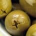 Close-up of green olives in a white bowl with a glossy surface. - Olive Oil Times