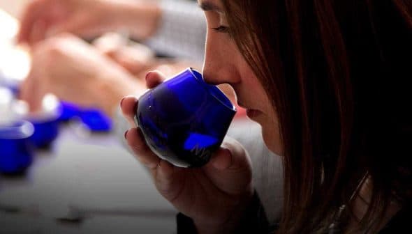 Individual smelling olive oil from a blue tasting cup during a tasting session. - Olive Oil Times