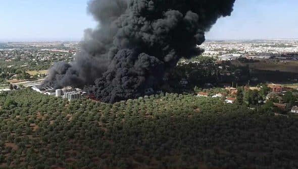 Thick black smoke rising from an industrial area surrounded by olive trees and buildings. - Olive Oil Times