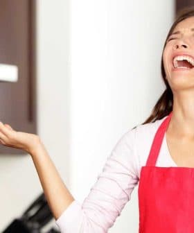 Woman wearing a red apron with a distressed expression in a kitchen setting. - Olive Oil Times