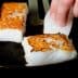 Person placing fish fillets into a skillet while cooking on a stovetop. - Olive Oil Times