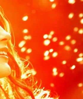 A woman smiling while holding a dandelion seed head in her hand, with a blurred background. - Olive Oil Times