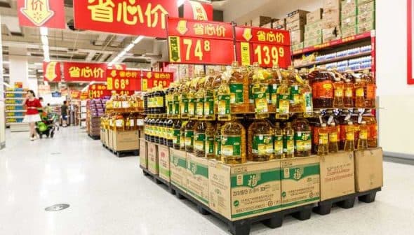 Rows of cooking oil bottles arranged on pallets in a supermarket aisle. - Olive Oil Times