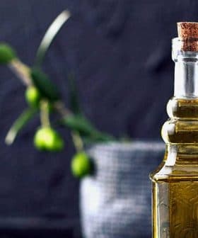 A glass olive oil cruet with a cork stopper, featuring a smooth design and filled with olive oil. - Olive Oil Times