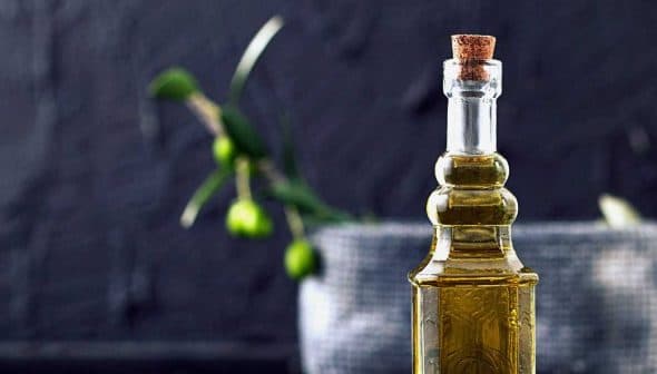 A glass olive oil cruet with a cork stopper, featuring a smooth design and filled with olive oil. - Olive Oil Times
