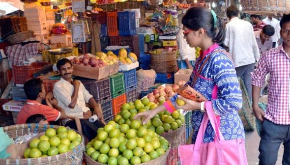 A woman selecting limes from a basket in a busy fruit market with people around her. - Olive Oil Times