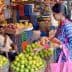 A woman selecting limes from a basket in a busy fruit market with people around her. - Olive Oil Times