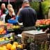 People shopping at an outdoor market with various fruits and vegetables displayed on tables. - Olive Oil Times