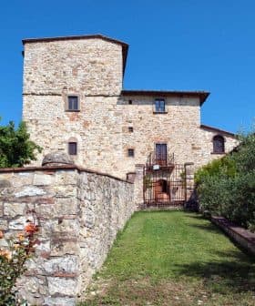 A stone building featuring a tower and surrounded by a garden with roses and greenery. - Olive Oil Times