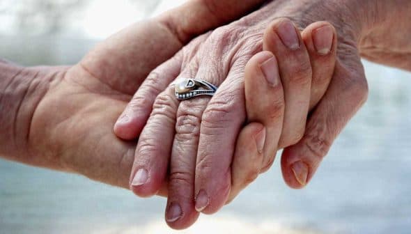 Close-up of two hands holding each other, one adorned with a silver ring. - Olive Oil Times