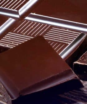 A dark chocolate bar with several pieces broken off, placed on a wooden surface. - Olive Oil Times