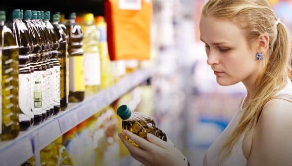 A woman inspecting a bottle of olive oil while shopping in a supermarket aisle. - Olive Oil Times