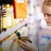 A woman inspecting a bottle of olive oil while shopping in a supermarket aisle. - Olive Oil Times