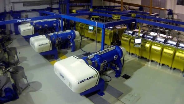 Industrial olive oil production equipment with blue and yellow machines in a processing facility. - Olive Oil Times