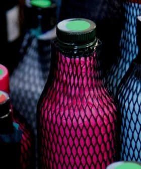Various bottles covered in mesh with colored caps and labels arranged closely together. - Olive Oil Times