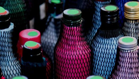 Various bottles covered in mesh with colored caps and labels arranged closely together. - Olive Oil Times