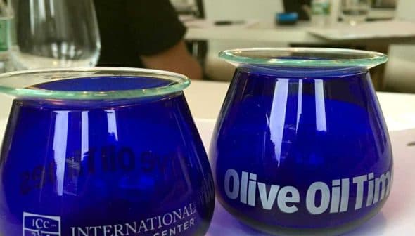 Two blue glass cups labeled 'International Culinary Center' and 'Olive Oil Times' on a table. - Olive Oil Times