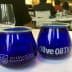 Two blue glass cups labeled 'International Culinary Center' and 'Olive Oil Times' on a table. - Olive Oil Times