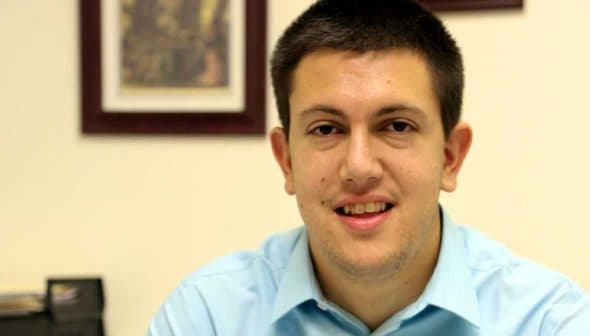 Young man with short dark hair wearing a light blue shirt, smiling at the camera. - Olive Oil Times