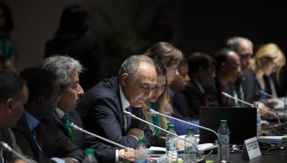 Group of officials seated at a conference table during a meeting, with a speaker addressing the group. - Olive Oil Times