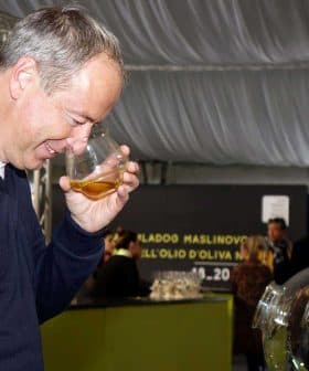 Man holding a glass of olive oil and smelling it during an event. - Olive Oil Times