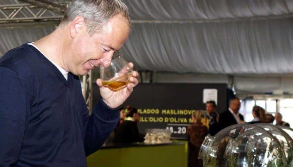 Man holding a glass of olive oil and smelling it during an event. - Olive Oil Times