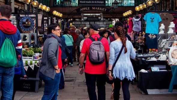 People walking through Apple Market with various stalls and merchandise on display. - Olive Oil Times