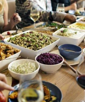A dining table filled with various dishes, including salads, meats, and side dishes, with people dining around it. - Olive Oil Times