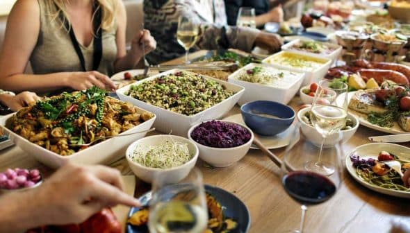 A dining table filled with various dishes, including salads, meats, and side dishes, with people dining around it. - Olive Oil Times