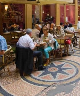 People dining at tables in a café with patterned flooring and an indoor setting. - Olive Oil Times