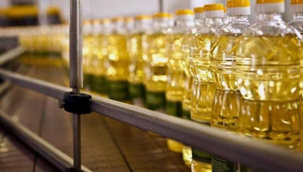 Rows of clear plastic bottles filled with cooking oil on a production line. - Olive Oil Times