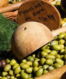 A collection of green olives displayed with wooden utensils and signs indicating prices. - Olive Oil Times