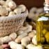 Glass bottle of peanut oil with a cork stopper next to a bowl of peanuts on a wooden surface. - Olive Oil Times