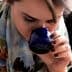Woman with a scarf smelling from a blue cup while holding a white lid and a pen. - Olive Oil Times