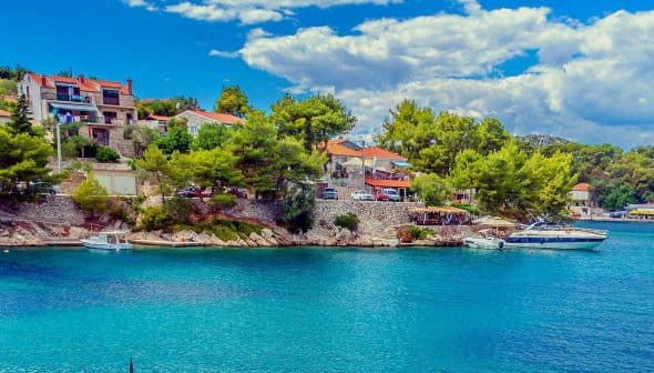 A coastal scene featuring houses on a hillside and boats in clear blue water. - Olive Oil Times