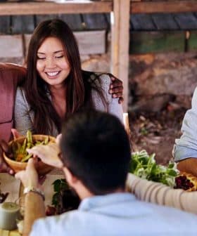 A diverse group of people sitting around a table sharing food in an outdoor setting. - Olive Oil Times