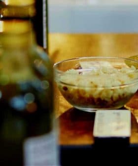 A person dipping bread into a bowl of olive oil for tasting at a display. - Olive Oil Times