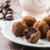 A plate of chocolate truffles coated in cocoa powder with one truffle partially bitten into. - Olive Oil Times