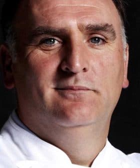 Portrait of a chef wearing a white uniform with a serious expression against a dark background. - Olive Oil Times