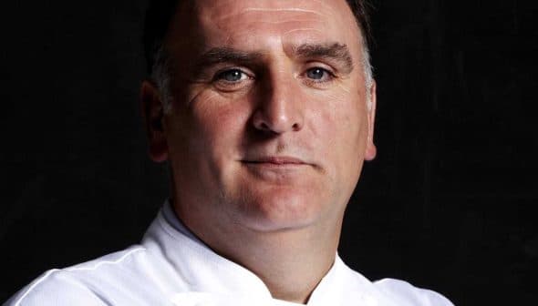Portrait of a chef wearing a white uniform with a serious expression against a dark background. - Olive Oil Times