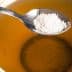 A spoon holding sugar above a cup of tea filled with a light brown liquid. - Olive Oil Times
