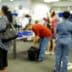 Blurred image of passengers and airport staff in a check-in area with luggage and service counters. - Olive Oil Times