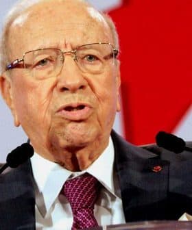 Elderly man in a suit speaking passionately at a podium with raised hands. - Olive Oil Times