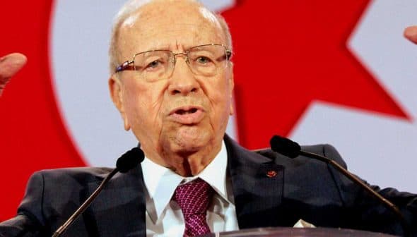 Elderly man in a suit speaking passionately at a podium with raised hands. - Olive Oil Times