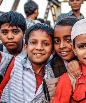 A group of seven children smiling at the camera, wearing school uniforms and backpacks. - Olive Oil Times