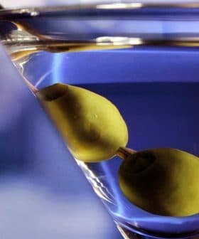 A close-up of a martini glass containing a clear drink and two green olives. - Olive Oil Times