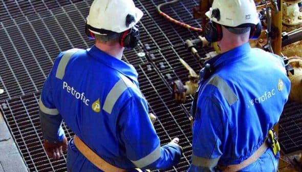 Two Petrofac workers wearing blue uniforms and safety helmets discussing on a metal grid surface. - Olive Oil Times