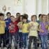 A group of children in colorful shirts singing together in a classroom setting. - Olive Oil Times