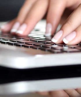 Close-up of hands typing on a laptop keyboard with a reflective surface. - Olive Oil Times